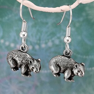 May include: A pair of silver dangle earrings featuring a detailed, three-dimensional sculpted image of a wombat.