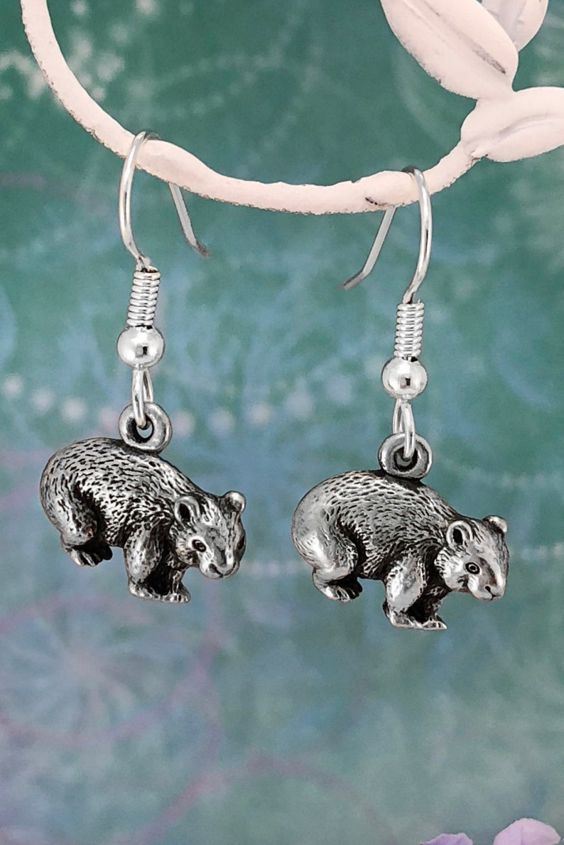 May include: A pair of silver dangle earrings featuring a detailed, three-dimensional sculpted image of a wombat.