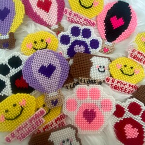 May include: A collection of colorful felt crafts featuring various designs, including smiley faces, paw prints, hot air balloons, and a slice of bread. The crafts have different phrases written on them, such as "I Love You", "Or My Squeezie", and "You Are My Main Squeezie".