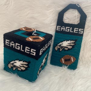 May include: A green, black, and white tissue box cover with an eagle and football design. The cover says "Eagles" on the front. A matching door hanger with the same design and the word "Eagles" is also included.