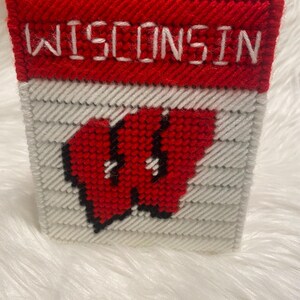 May include: A red and white cross-stitch with the word "WISCONSIN" in white lettering and a red "W" logo.