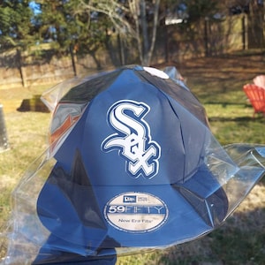 May include: A blue and white baseball cap with a white "S" logo and the text "New Era 59FIFTY" on the front. The cap is in a plastic bag.