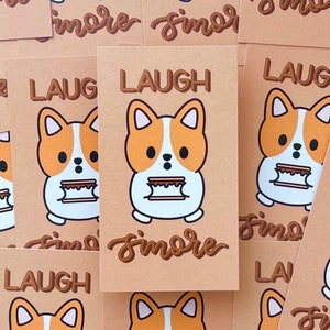 以下が含まれることがあります： スモアを持っている漫画のコーギーが描かれた茶色のカード10枚セット。カードには「Laugh s'more」と書かれています。