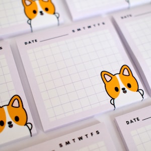 May include: A stack of light purple memo pads with a grid pattern and a cute cartoon corgi dog illustration. Each pad has the days of the week and a date line. The corgi is orange, white, and black.
