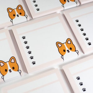 Könnte beinhalten: Ein Set aus rosa und weißen Notizblöcken mit einer niedlichen Cartoon-Corgi-Hund-Illustration und Pfotenabdruck-Designs.