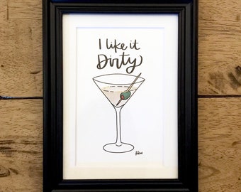 May include: A black framed print with a white background. The print features a martini glass with an olive and a handwritten phrase that says "I like it Dirty".