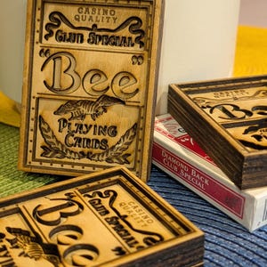 May include: Two rectangular wooden boxes with laser-engraved designs mimicking Bee playing card packaging, featuring the text Casino Quality, Club Special, Bee, and Playing Cards. A standard red and white Diamond Back Club Special deck is visible.