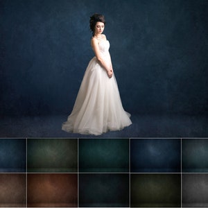 May include: A woman in a white wedding dress stands in front of a dark blue textured background. The dress has a sweetheart neckline and a fitted bodice. The skirt is full and flowing, and the woman is wearing her hair up in a bun.