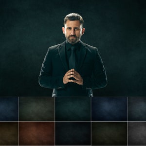 May include: A man in a black suit with a black tie stands against a dark background. He has a serious expression on his face and his hands are clasped in front of him.
