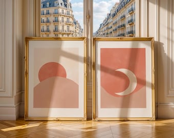 Puede incluir: Dos impresiones de arte abstracto enmarcadas con un diseño minimalista. La impresión de la izquierda presenta un sol de color melocotón poniéndose detrás de una colina de color melocotón. La impresión de la derecha presenta una luna creciente blanca sobre un fondo de color melocotón.