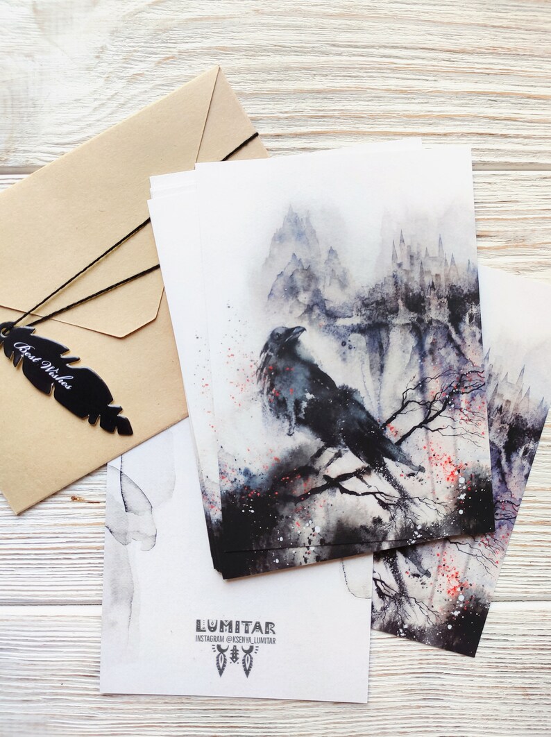 Puede incluir: Un conjunto de cuatro postales de acuarela con un cuervo negro posado en una rama frente a un paisaje monta&ntilde;oso brumoso. Las tarjetas est&aacute;n impresas con el nombre de usuario de Instagram del artista, "@KSENYA_LUMITAR", y la palabra "LUMITAR".