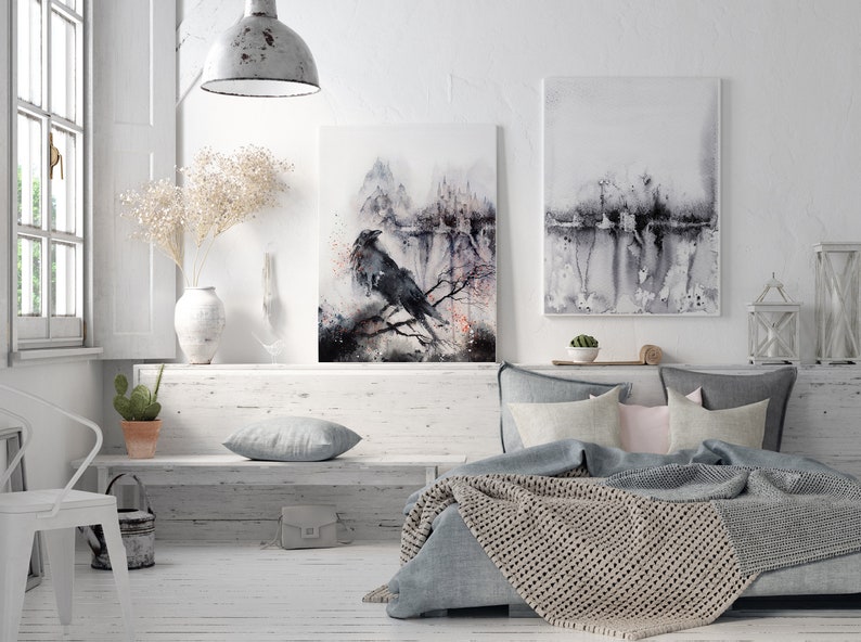 Puede incluir: Un dormitorio blanco con una cama, un banco y dos acuarelas en la pared. La pintura de la izquierda presenta un cuervo negro posado en una rama en un bosque brumoso. La pintura de la derecha es una acuarela m&aacute;s abstracta de una escena de bosque.