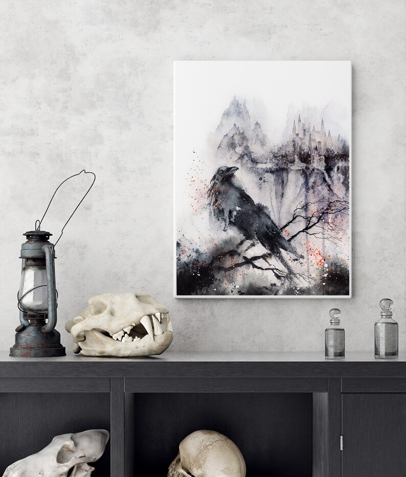 Puede incluir: Una pintura de acuarela de un cuervo posado en una rama frente a una cadena monta&ntilde;osa brumosa con un castillo en el fondo. La pintura est&aacute; enmarcada en un marco blanco y est&aacute; colgada en una pared gris.