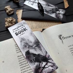 Puede incluir: Un marcap&aacute;ginas en blanco y negro con una ilustraci&oacute;n de acuarela de un cuervo posado en una rama. El marcap&aacute;ginas tiene el texto "everything starts with BOOK" en letras negras.