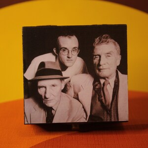 May include: Black and white photo of three men. The man in the center is wearing glasses and a light-colored shirt. The man on the left is wearing a hat and a dark suit. The man on the right is wearing a dark suit and tie.