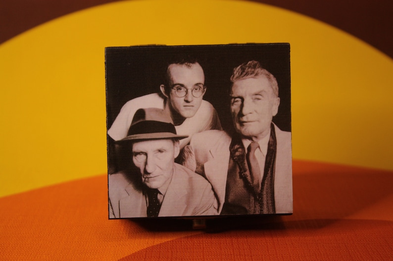 May include: Black and white photo of three men. The man in the center is wearing glasses and a light-colored shirt. The man on the left is wearing a hat and a dark suit. The man on the right is wearing a dark suit and tie.