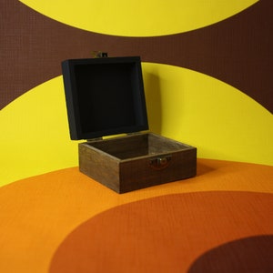 May include: An open wooden box with a black interior. The box is sitting on a yellow, orange, and brown patterned surface.