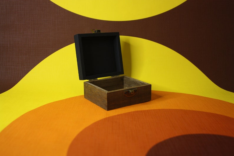 May include: An open wooden box with a black interior. The box is sitting on a yellow, orange, and brown patterned surface.