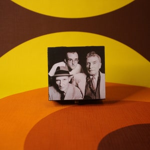 May include: A black and white photo of three men in suits and hats. The photo is framed in a black box.