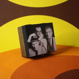 May include: A wooden box with a black and white photo of three men. The men are wearing hats and suits. The box is sitting on a brown and yellow patterned surface.