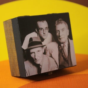 May include: A black and white photo of three men in a wooden frame. The men are wearing suits and hats. The photo is on a yellow and orange surface.