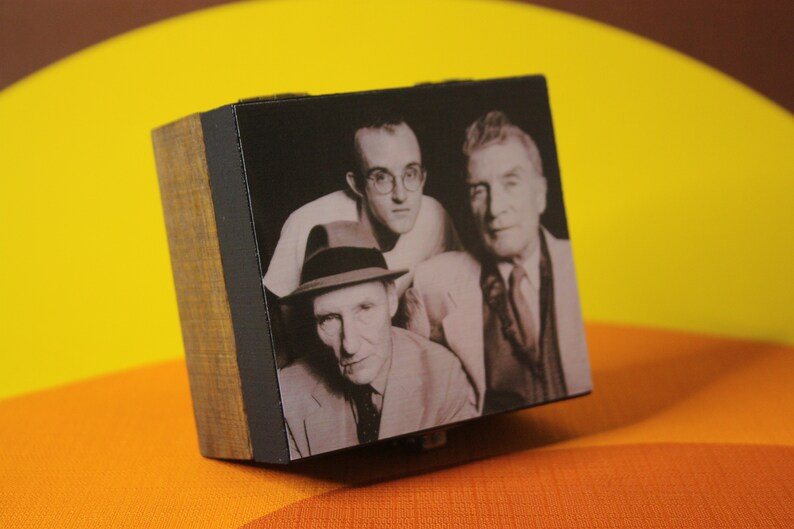 May include: A black and white photo of three men in a wooden frame. The men are wearing suits and hats. The photo is on a yellow and orange surface.