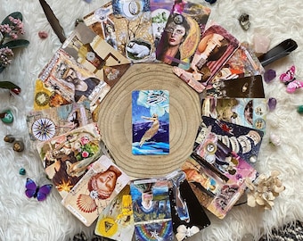 Puede incluir: Un conjunto de cartas de tarot dispuestas en semicírculo sobre una rodaja de madera, con una carta central que muestra a una mujer con un vestido fluido. Las cartas exhiben diversas ilustraciones y texto, con elementos decorativos como plumas y cristales.