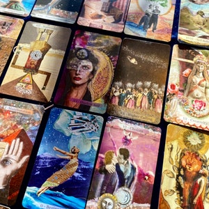 May include: A collection of tarot cards with various illustrations and text. The cards feature images of figures, celestial bodies, and symbolic elements. The color palette includes gold, blue, and earth tones. The cards are arranged on a dark blue surface.