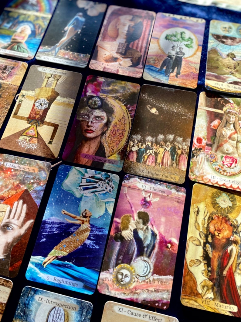 May include: A collection of tarot cards with various illustrations and text. The cards feature images of figures, celestial bodies, and symbolic elements. The color palette includes gold, blue, and earth tones. The cards are arranged on a dark blue surface.