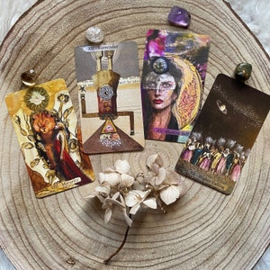 May include: Four tarot cards with illustrations and text, including "VIII - Maturity", "XII - Surrender", "XV - Shadow Self", and "XX - Higher Calling". The cards are arranged on a wooden surface with crystals and dried flowers.