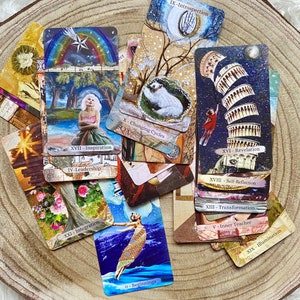 May include: A collection of tarot cards with various illustrations and text. The cards feature images of a rainbow, a woman, a leaning tower, and other symbolic imagery. Text includes "Inspiration", "Beginnings", and "Revelation".