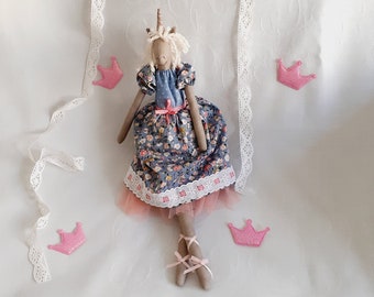 May include: A handmade unicorn doll wearing a blue and floral dress with a pink tulle skirt and white lace trim. The doll is sitting on a white sheet with pink crowns scattered around it.