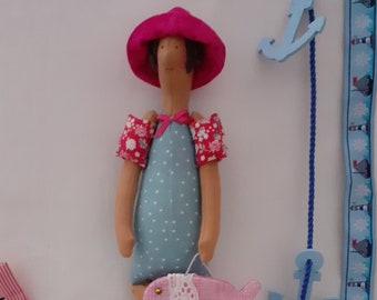 May include: A handmade doll wearing a pink hat, blue and white polka dot swimsuit, and pink arm floaties. The doll is holding a pink fish with a white lace trim.