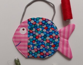 May include: A pink and blue fish-shaped fabric bag with a gray handle. The bag is decorated with a pattern of scales and stripes. Three spools of thread are visible in the image: red, green, and olive green.