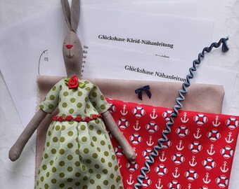 May include: A gray fabric bunny doll wearing a green polka dot dress with red trim. The doll is surrounded by fabric scraps with a red and white anchor and life preserver pattern.