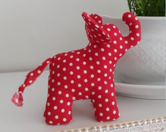 Könnte beinhalten: Rotes Stoffelefantenspielzeug mit weißen Punkten. Der Elefant hat einen eingerollten Rüssel und einen langen Schwanz.