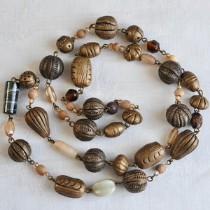 May include: A long necklace made of brown and gold beads. The beads are various shapes and sizes, including round, oval, and rectangular. Some of the beads have intricate designs.