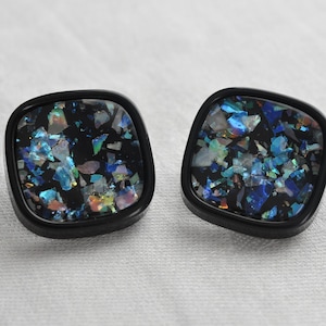 May include: A pair of black square-shaped earrings with iridescent blue and green glitter embedded in the centre of each earring.