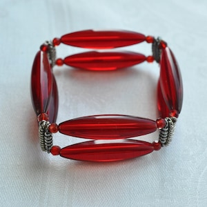 Op de afbeelding: Een rode kralen armband met zilveren accenten. De armband is gemaakt van ovale kralen en heeft een elastisch elastiek.