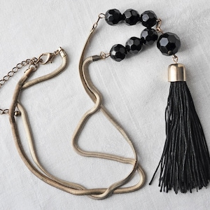 May include: A gold chain necklace with a black tassel pendant. The pendant is made of black beads and has a gold cap.