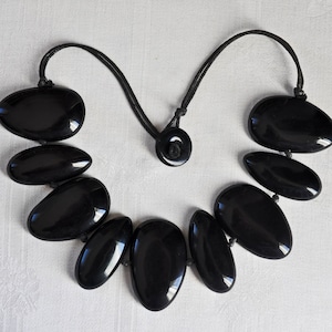 Ras de cou en perles de bakélite noires.  Collier de perles asymétriques Early Sobral.  Plat d&#39;un côté, bombé de l&#39;autre, enfilé sur des cordons en coton épais, années 60-70