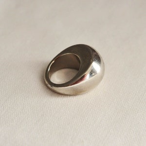 May include: A silver ring with a smooth, rounded top. The ring is made of metal and has a simple, modern design.