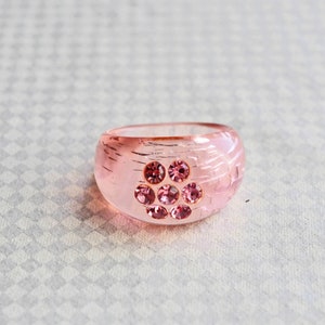 May include: A pink ring with a clear, textured band and a cluster of pink rhinestones in the centre.