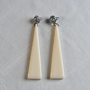 Könnte beinhalten: Ein Paar weiße, dreieckige Ohrhänger mit silbernen Glitzer-Oberteilen.