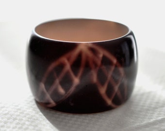 Wide, over dyed, deep maroon Lucite, bangle.  Leaf shaped silhouettes zig zag around the bangle, bracelet.  Hippie Boho Deco Revival bangle.