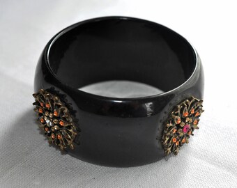 Wide, Art Deco Lucite bangle, bracelet.  Slightly domed, jet black, with 4 metal flower motifs attached on 4 flattened sides.  1930s bangle.