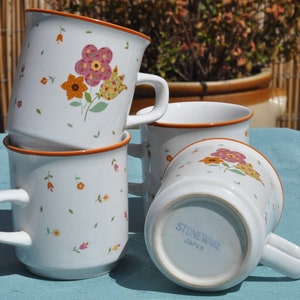 May include: Four white ceramic mugs with floral designs. The mugs are stacked on top of each other. The bottom mug has the words "Stoneware Japan" printed on the bottom.
