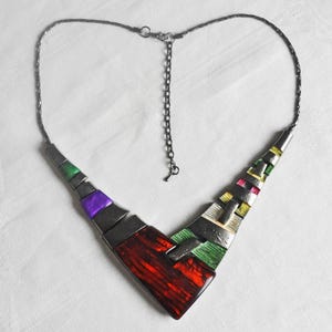 Könnte beinhalten: Eine geometrische Statement-Halskette mit V-förmigem Design. Die Halskette ist aus Metall und verfügt über farbige Emaille-Akzente in Rot-, Grün-, Lila- und Gelbtönen.