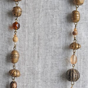 May include: Two strands of beads with a variety of materials, including wood, glass, and metal. The beads are strung on a chain and are arranged in a symmetrical pattern. The beads are a mix of brown, gold, and clear colors.