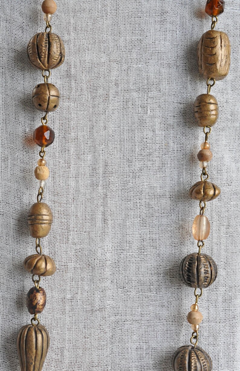May include: Two strands of beads with a variety of materials, including wood, glass, and metal. The beads are strung on a chain and are arranged in a symmetrical pattern. The beads are a mix of brown, gold, and clear colors.